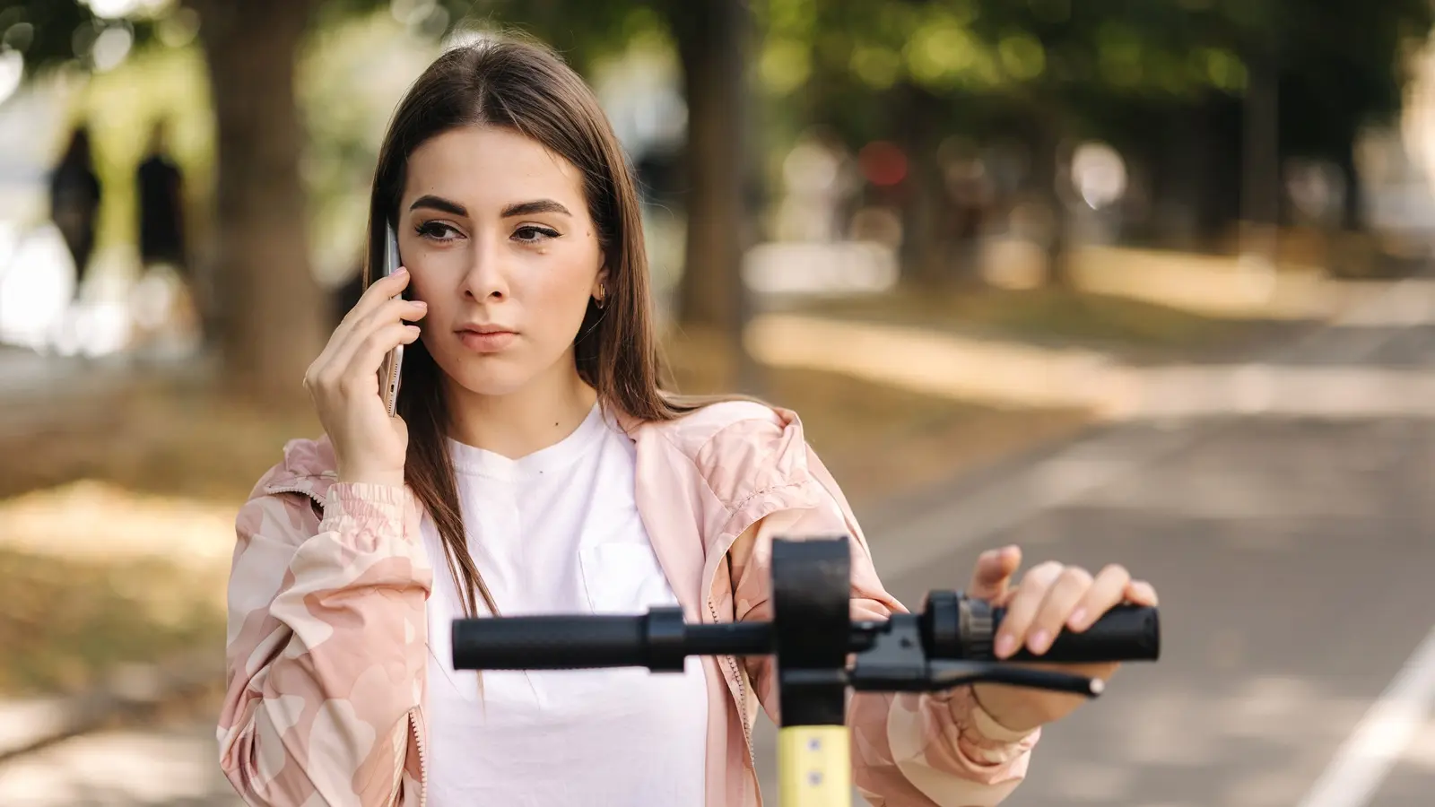 Eine junge Frau fährt E-Scooter und hält dabei ein Smartphone in der Hand.