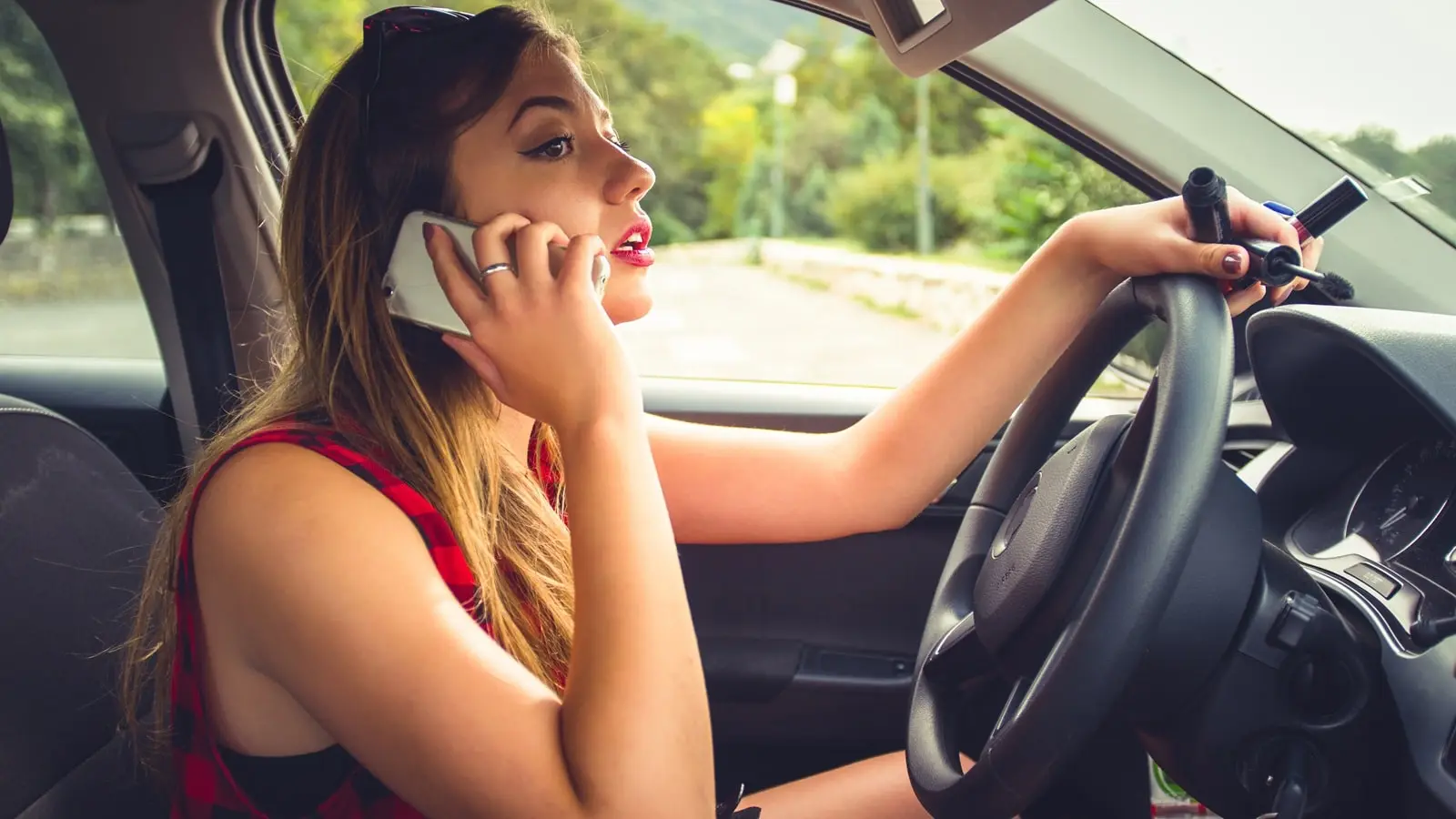 Eine junge Autofahrerin telefoniert mit Ihrem Smartphone während der Fahrt.