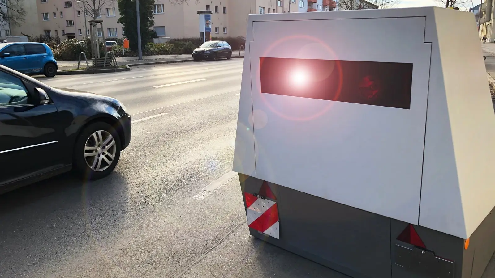 Ein moderner Blitzeranhänger steht in einer Innenstadt und blitzt ein Auto.